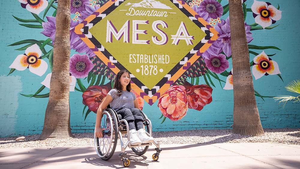 girl in wheelchair in front of Mesa sign