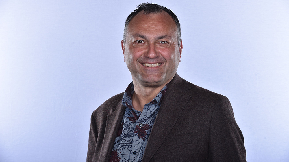 smiling man in dark jacket and blue print shirt