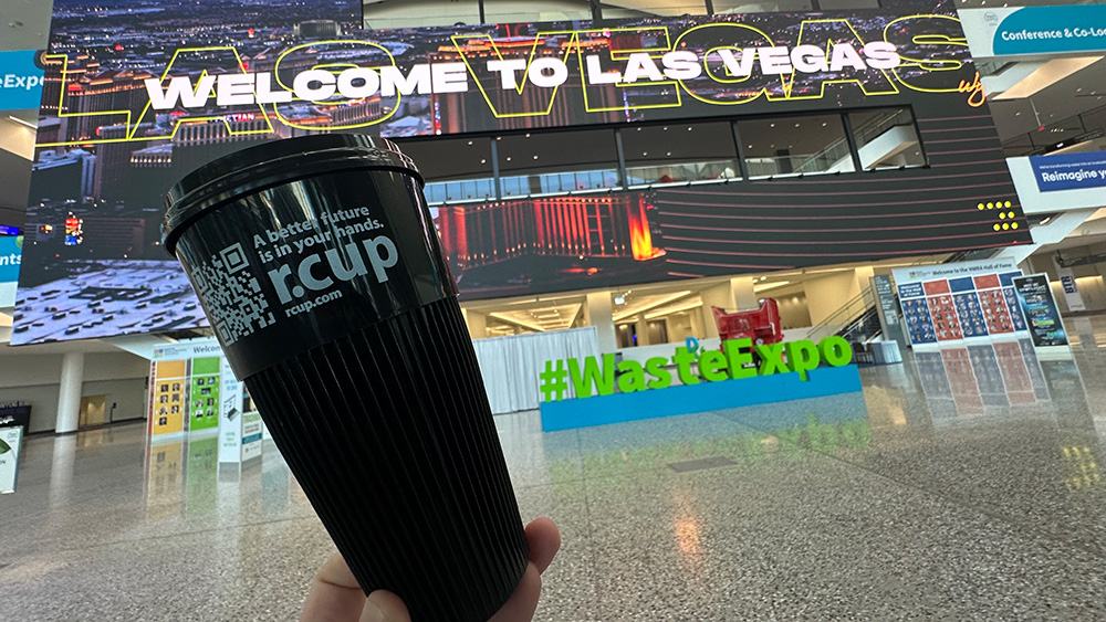 hand holding reusable cup in front vegas sign in expo hall