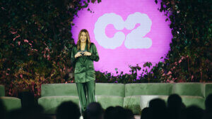 woman speaking with C2 sign behind her