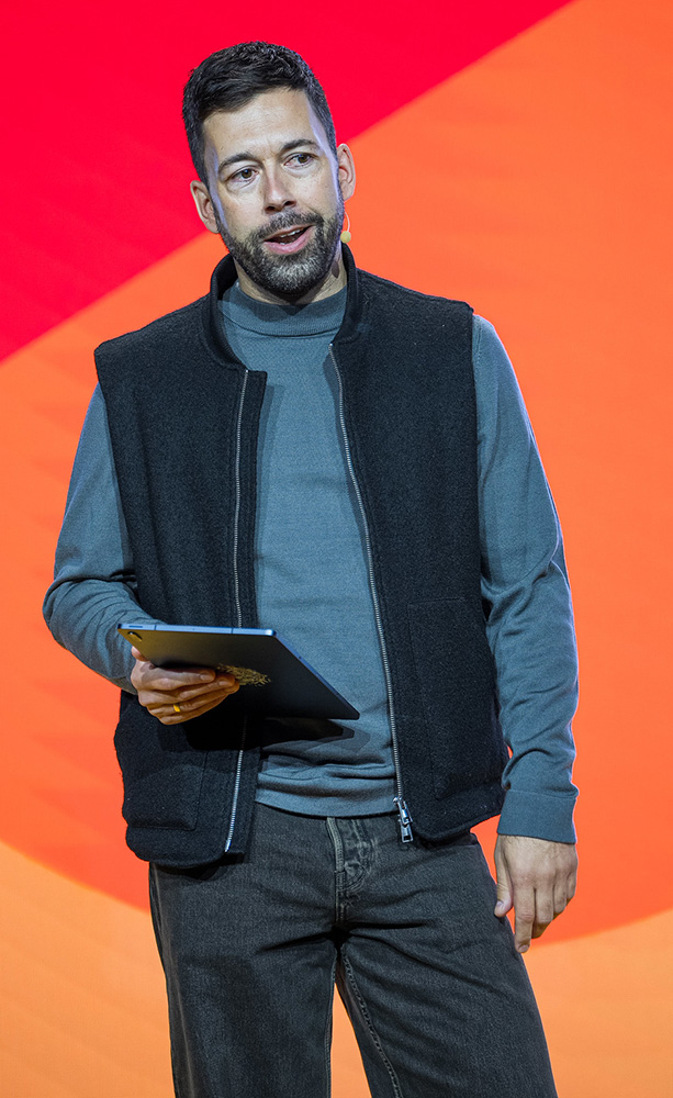 man in grey shirt and black vest speaking