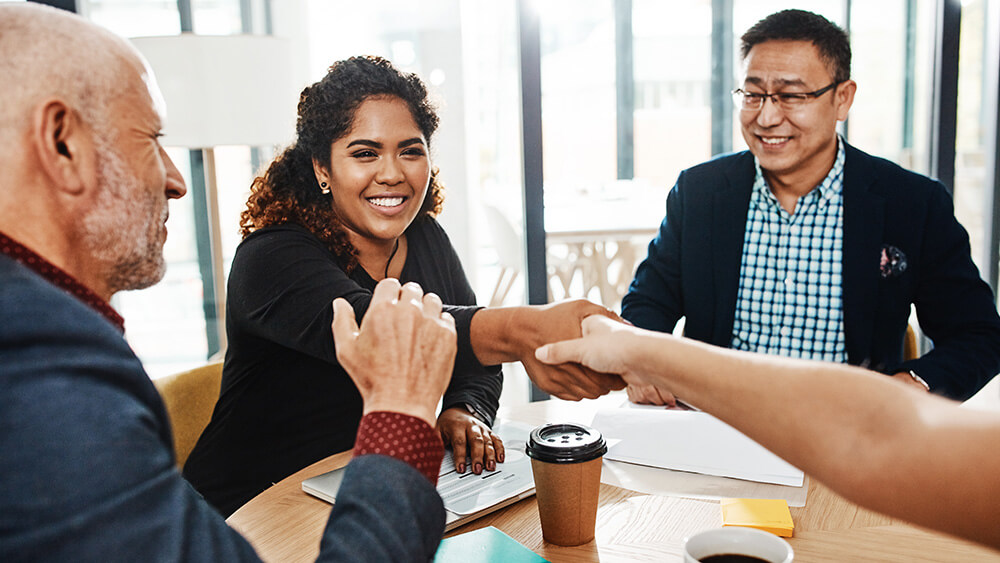 woman of color shaking hands with someone as two men watch at conference table